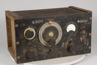 Audio instrument, oscillator. Large rectangular body, wood frame on sides, black front panel and decorative grill on to pand back. On front panel, large dials, circular window for meter, pair of electrical connectors, indicator light and switches.